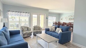 En stue med en blå sofa, mønstrede lænestole, et sofabord og et spiseområde med træstole og et bord.