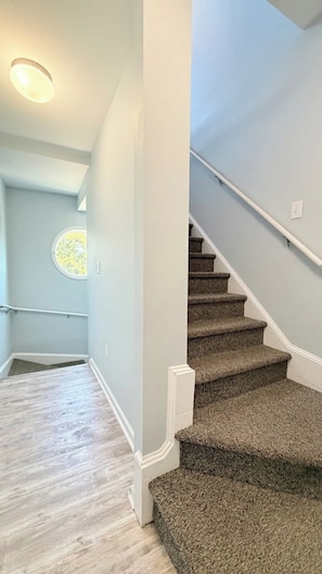 Una escalera con escalones alfombrados y barandal, que lleva a una plataforma con una lámpara.