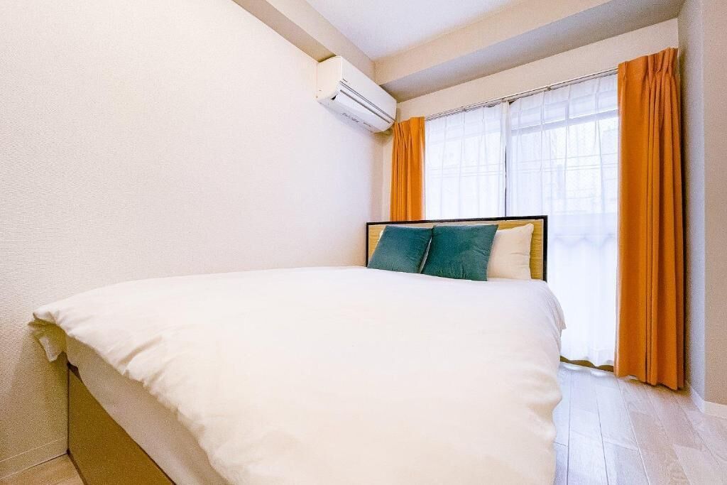 A bedroom with a bed, an air conditioning unit, a window with curtains, and a wooden floor.