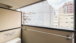 Une fenêtre dotée d’une rambarde de sécurité en métal, une enseigne en japonais et une vue sur des immeubles.