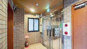 Un hall d’hôtel avec des murs recouverts de carreaux, un extincteur, une porte en verre et un panneau indiquant la sortie de secours.