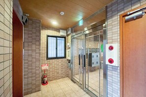 Eine Hotelhalle mit Fliesenwänden, einem Feuerlöscher, einer Glastür und einem Notausgangsschild.