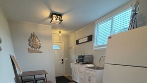 A compact kitchen with white cabinets, a refrigerator, a microwave, and a dining area with a small table and chairs.