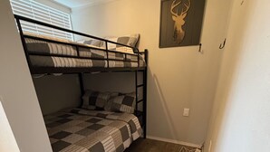 A bunk bed room with a checkered bedspread, a deer wall art, and wooden flooring.