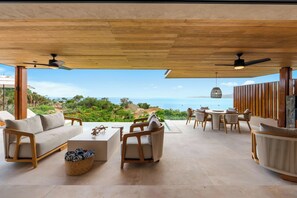 A spacious outdoor seating area with a view of the ocean, wooden furniture, and ceiling fans. - Ocean-View Iyari Villa, Pool, Cook & Golf Cart (Corral del Risco)