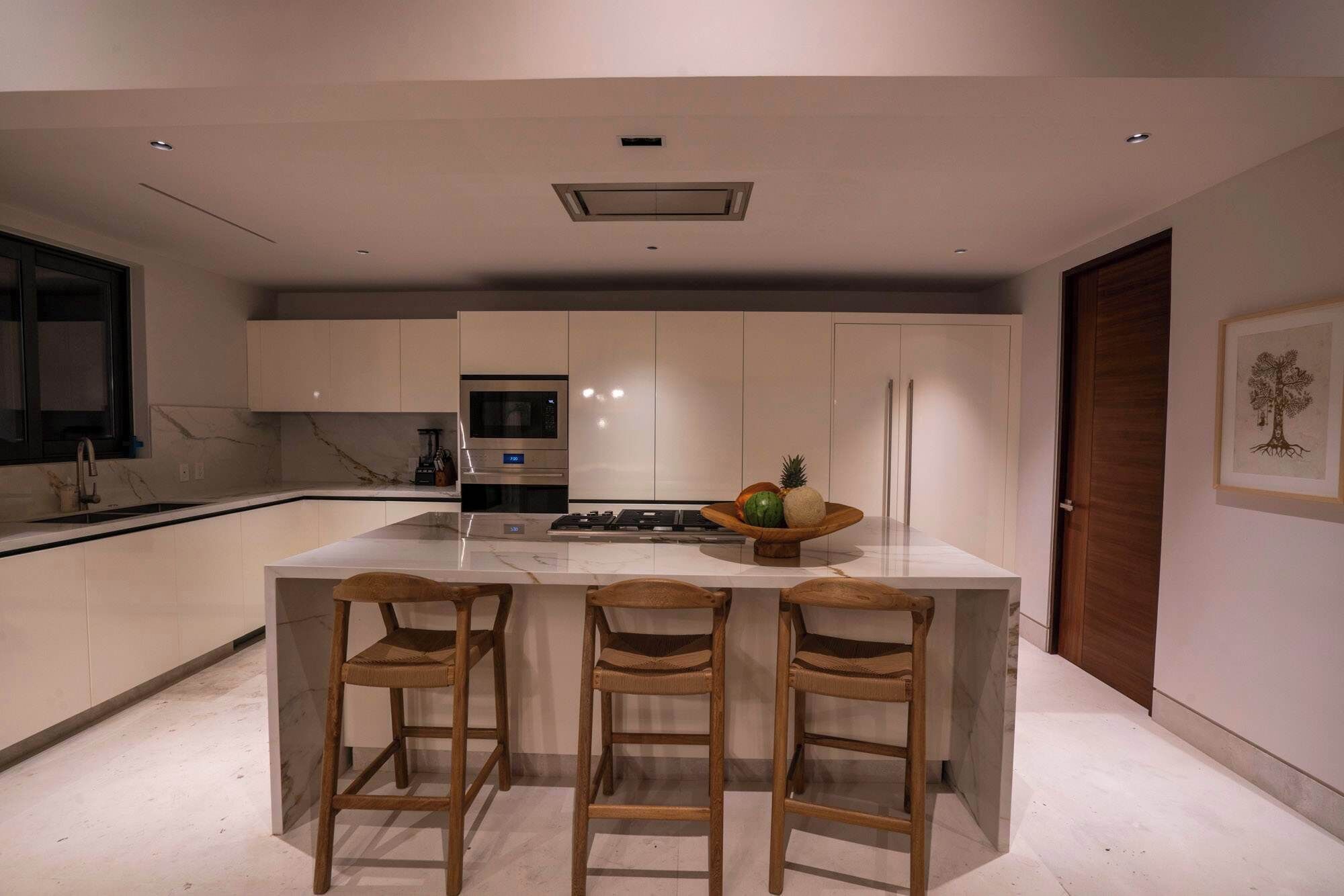 A modern kitchen with a central island, bar stools, a microwave, and a refrigerator.
