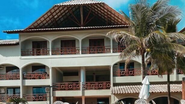 A pool with lounge chairs, a building with balconies, and palm trees. - Hotel privê do Atalaia  (Salinópolis)