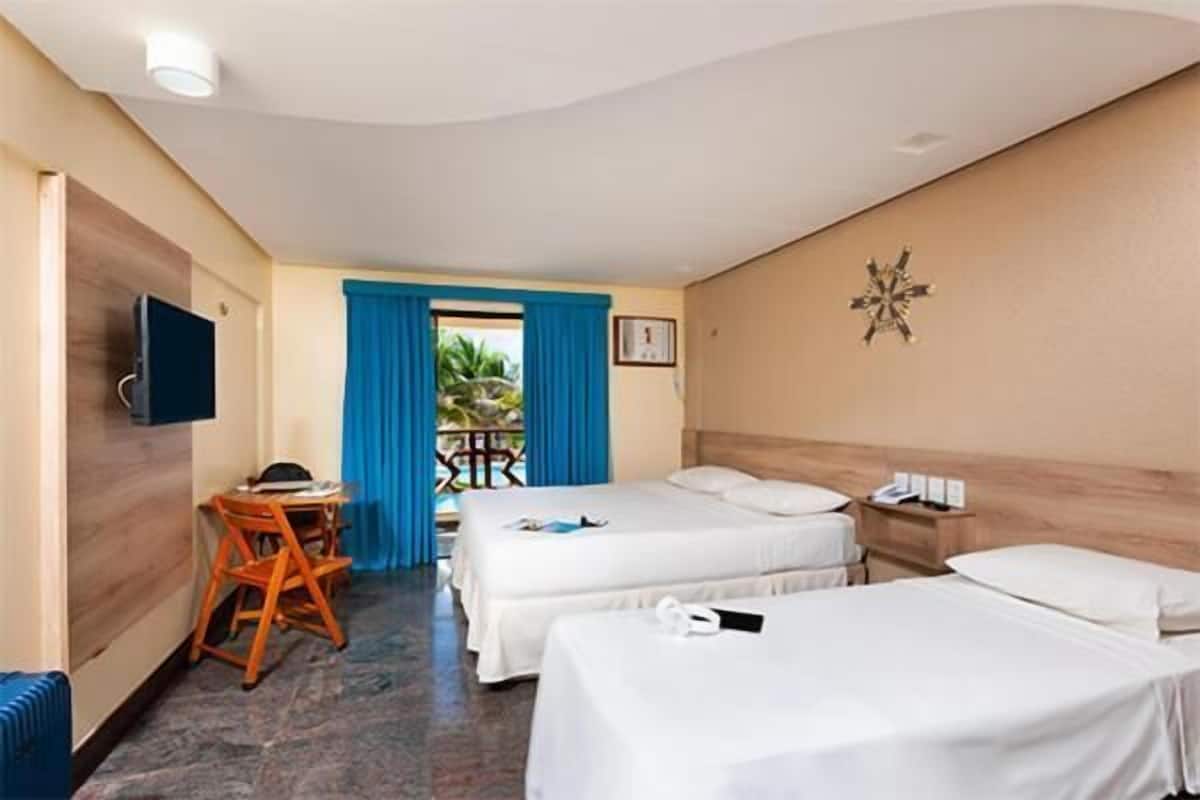 Une chambre d’hôtel avec deux lits, un bureau, une chaise, une télévision et un balcon avec des rideaux bleus.