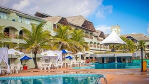 A pool area with a clear blue pool, white lounge chairs, and umbrellas. - Hotel privê do Atalaia  (Salinópolis)