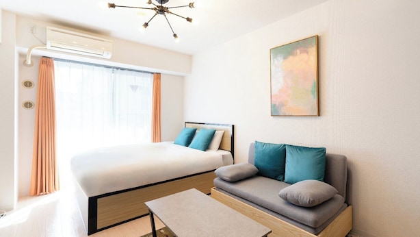 Una camera d'albergo con un letto, un divano, un tavolo, un condizionatore d'aria e una ventola a soffitto.