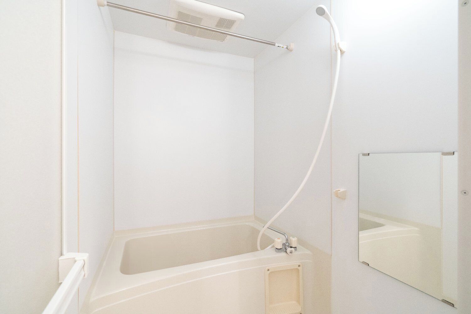 A white bathroom with a bathtub, a showerhead, and a mirror.