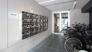 Un corridoio con una fila di armadietti, un cartello con la scritta 'MAT OSAKA' e biciclette parcheggiate a destra.
