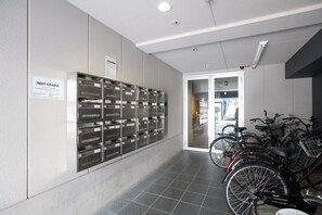 A hallway with a row of storage lockers, a sign reading 'MAT OSAKA,' and bicycles parked to the right. - Best Residence Kujo (Osaka)