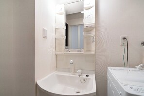 A small bathroom with a sink, mirror, and a washing machine. - Best Residence Kujo (Osaka)