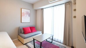 Una moderna camera d'albergo con divano, un tavolino, una TV a schermo piatto e un'ampia finestra con tende.