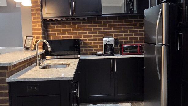 A modern kitchen with black cabinets, a stainless steel refrigerator, a microwave, and a coffee maker. -  Spacious Private Suite in Gainesville • Separate Entrance • WiFi • Washer/Dryer (Gainesville)
