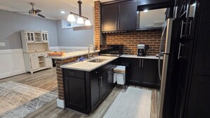 A modern kitchen with a brick backsplash, black cabinets, a microwave, and a coffee maker. -  Spacious Private Suite in Gainesville • Separate Entrance • WiFi • Washer/Dryer (Gainesville)