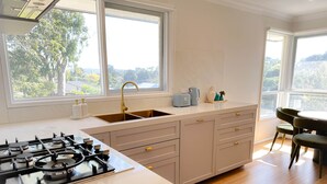Une cuisine moderne équipée d’une cuisinière à gaz, d’un évier double et offrant une vue sur l’extérieur grâce à de grandes fenêtres.