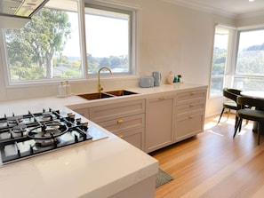 A modern kitchen with a gas stove, double sink, and a view of the outdoors through large windows. - The Contemporary Nest by Shine Mooroolbark (Mooroolbark)
