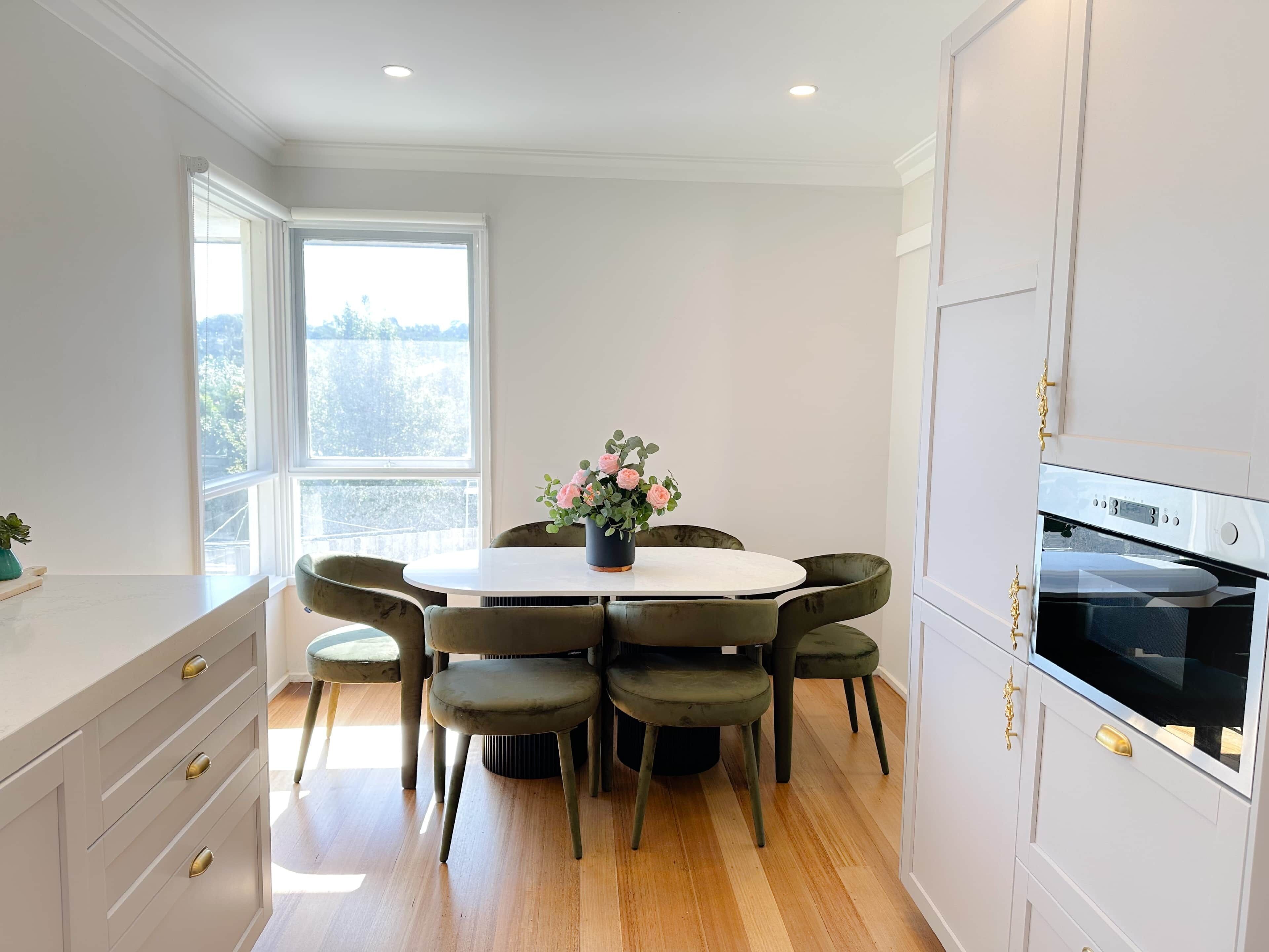 A modern kitchen with a round dining table, six chairs, a potted plant, and a built-in oven.