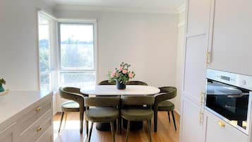 A modern kitchen with a round dining table, six chairs, a potted plant, and a built-in oven.