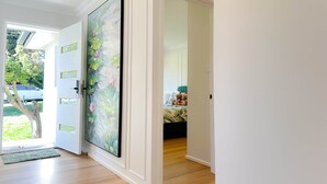 Un couloir avec une grande peinture florale sur la porte, un plancher en bois et une vue sur une chambre à coucher avec un lit et des peluches.