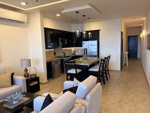 Una sala de estar moderna con un sofá, una mesita de centro y un comedor con sillas, y una cocina al fondo.