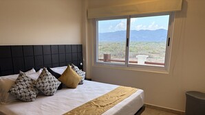 A bed with patterned pillows, a beige throw, and a view of a desert landscape through a window. - One Bedroom Oceanfront - Puerto Escondido 1423 (Bajos de Chila)