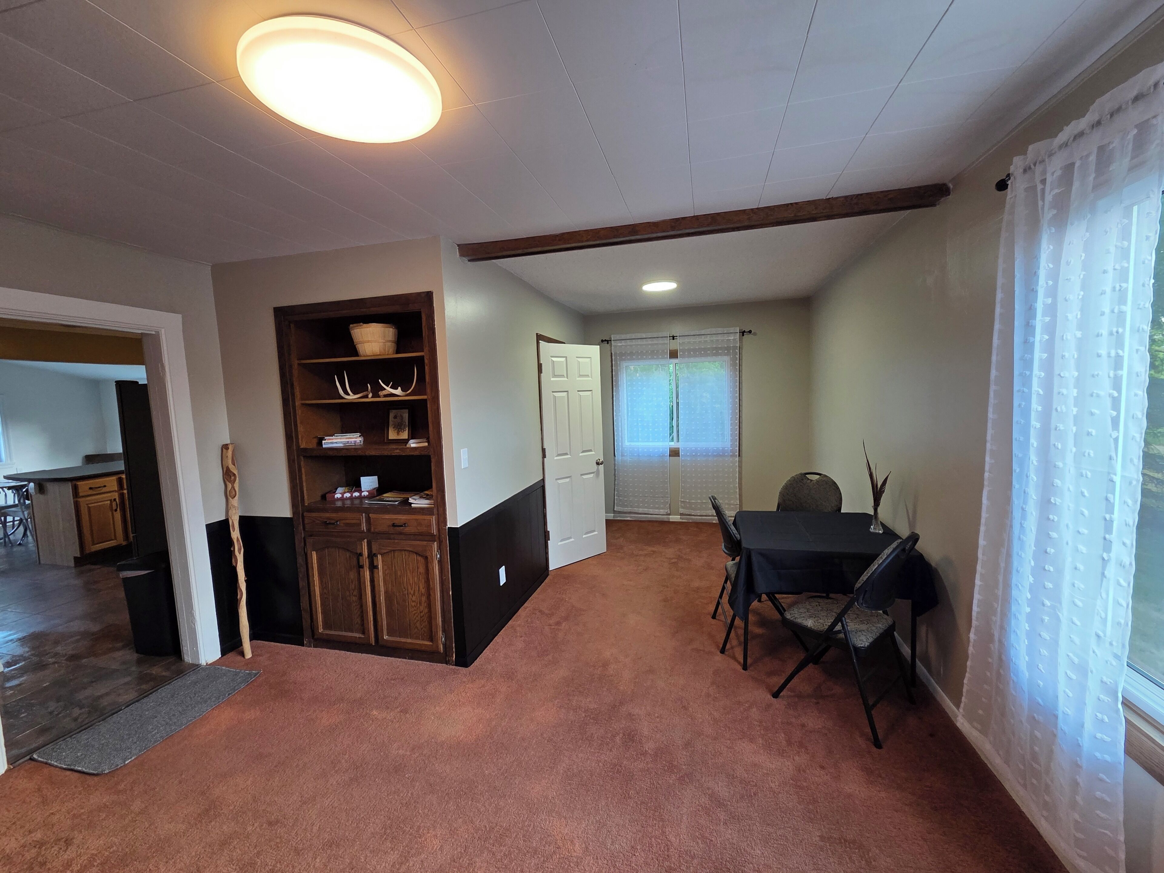 A room with a dining table, chairs, a wooden cabinet, a door, and a window with curtains.
