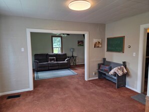 A living room with a brown carpet, a brown sofa, a small table, a bench, and a chalkboard with 'Welcome to Highland Heights' written on it.