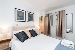 A hotel room with a bed, two framed pictures, a window with curtains, a bedside lamp, and a mirror. - Stylish 1BR Flat in Hull City Centre (Hull)