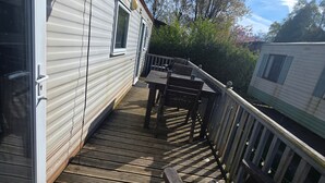 Un étroit couloir extérieur, délimité par une clôture en bois, surmonté d’un toit en métal et équipé d’une antenne parabolique.