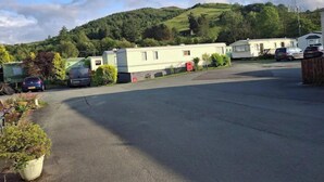 Un terrain de camping pour caravanes comprenant plusieurs caravanes, un espace de stationnement et un paysage vallonné en arrière-plan.