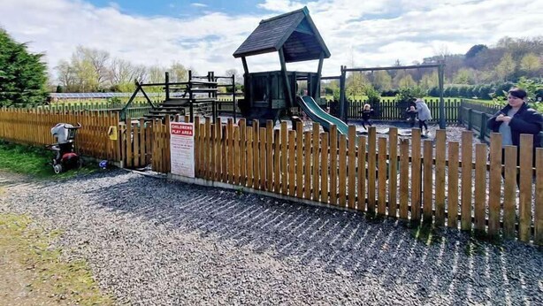 Une aire de jeux avec un toboggan et des structures d’escalade, entourée d’une clôture en bois.