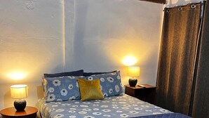 A bedroom with a bed, two bedside tables, a lamp on each table, and a curtain on the window. - In Front of the Beach! Spacious 4-bedroom villa in charming Sonsonate with AC. (Sonsonate)