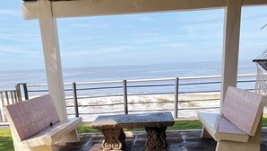A covered patio with stone flooring, two cushioned chairs, and a stone table. - In Front of the Beach! Spacious 4-bedroom villa in charming Sonsonate with AC. (Sonsonate)