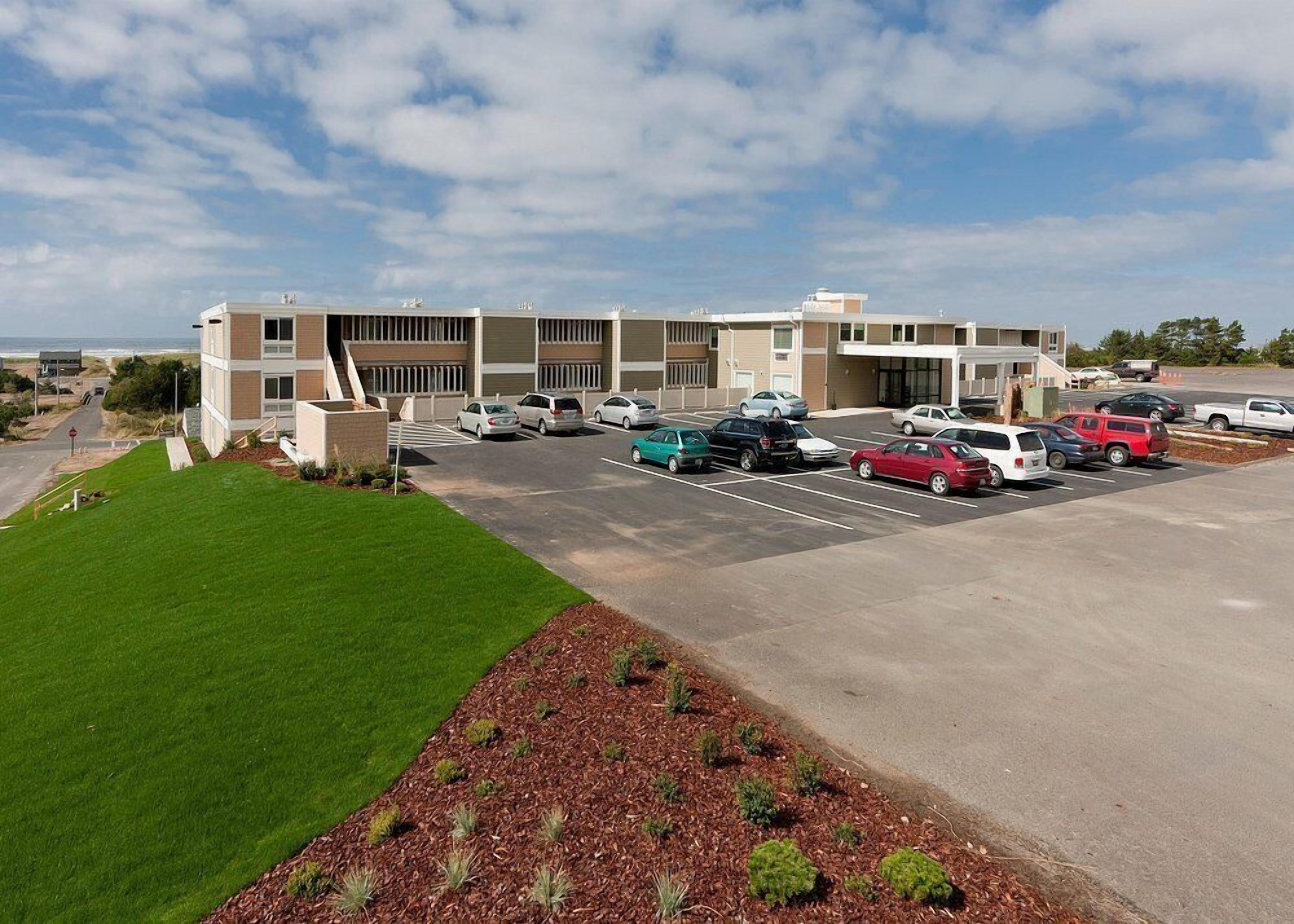 A modern building with a parking lot, a grassy area, and a clear sky.