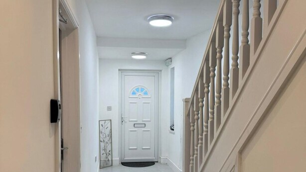 Een hal met een witte deur, een trap met witte spijlen en een plafondlamp.