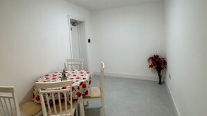 Een eetgedeelte met een ronde tafel, witte stoelen en een tafelkleed met bloemen.