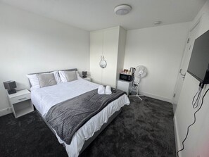 A hotel room with a bed, bedside tables, a TV, a microwave, and a fan. - Near Heathrow - Studio - WiFi - Parking - Sleeps 2 (Uxbridge)