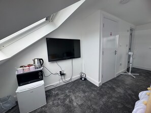 A small, modern room with a flat-screen TV mounted on the wall, a compact refrigerator, a coffee maker, and a power strip on the floor. - Near Heathrow - Studio - WiFi - Parking - Sleeps 3 (Uxbridge)