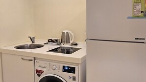Cocina compacta con lavadora, refrigerador y tetera sobre la encimera.