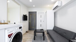 Un espacio habitable pequeño con lavadora, sofá, una mesita y una puerta.