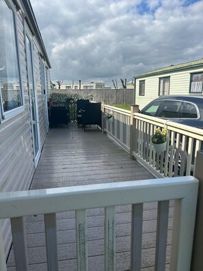 Ein überdachter Außenbereich mit Holzdeck, weißer Geländer und Kübelpflanzen.