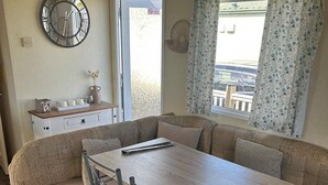 Una sala acogedora con un conjunto de sofás, una mesa de comedor y un reloj en la pared.