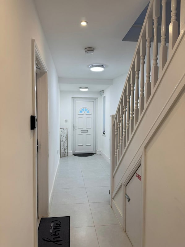 A hallway with a white door, a doormat, a staircase with white balusters, and a ceiling light.