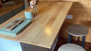 Une cuisine avec un plan de travail en bois, un évier, un vase de fleurs, une petite table et un tabouret.