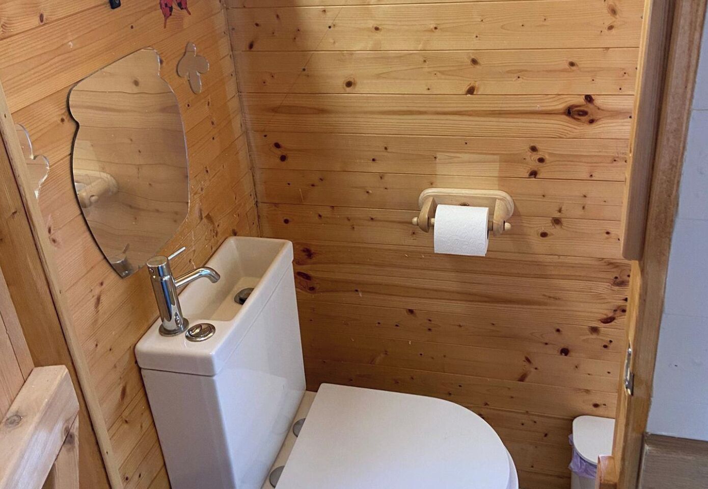 Ein kleines Badezimmer aus Holz mit Waschbecken, Toilette und Spiegel.
