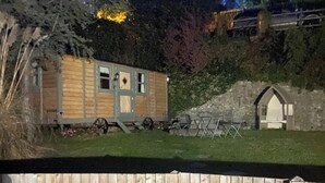 Une petite cabane en bois avec un porche, un petit abri de jardin et une cour clôturée.