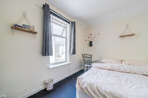 Ein Schlafzimmer mit zwei Betten, einem Fenster mit Vorhängen, einem Sessel, einem kleinen Tisch und Wanddekorationen.